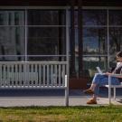 student sitting on a bench on campus and using a laptop