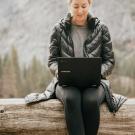 Individual sitting outdoors with laptop and winter coat