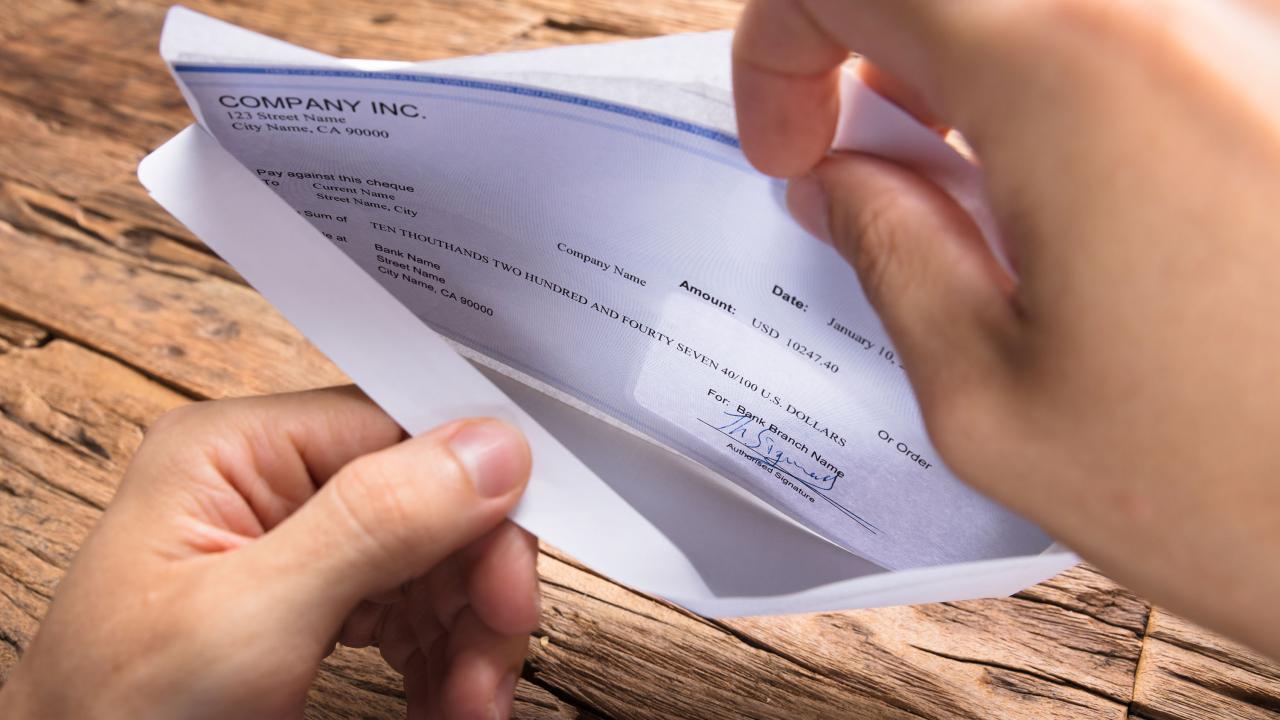 hands opening paycheck in envelop
