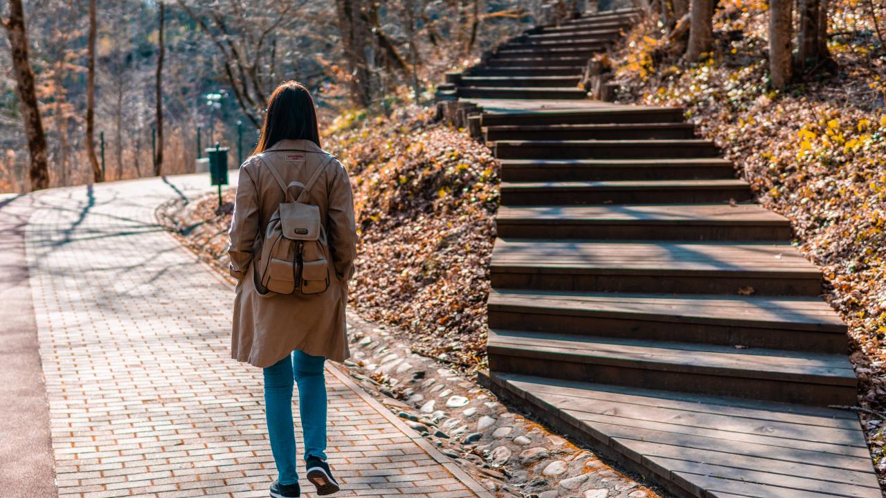 Student walking outdoors on a path, stairs off to the side