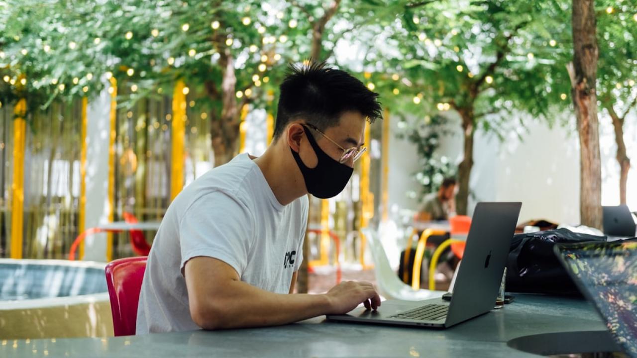 Person wearing face covering looking at laptop.